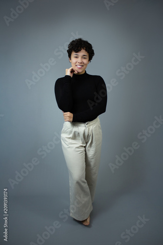 Full length portrait of beautiful young woman with short hair, posing graciously.  Studio shot with copy space on gray background, great for gen Z content, happiness, fashionable lady, and young adult