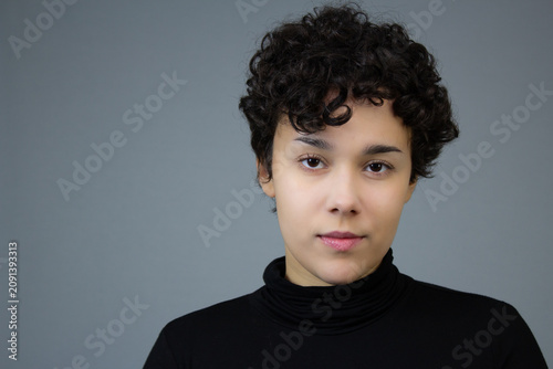 Headshot of a serious young lady with short hair. Horizontal studio portrait with copy space, ideal for gen z issues, content for woman, female individuality, and women empowerment.