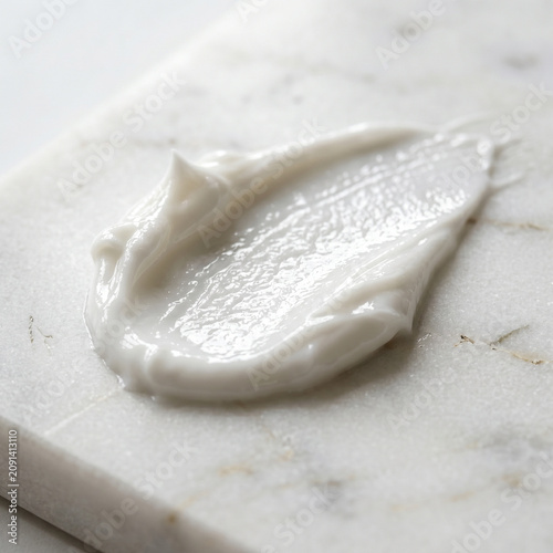 Macro of face cream smear with glossy texture on white marble