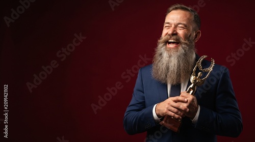 Happy older man with a trophy in a suit against a dark background  