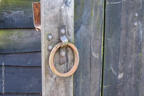 Fotografie a circular metal ring handle attached to a weathered, dark wooden gate
