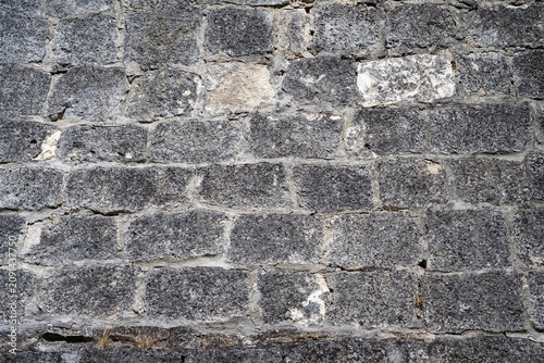 Fotografie a weathered, dark grey stone wall featuring roughly hewn rectangular blocks and light grey mortar