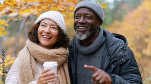 Smiling couple enjoying autumn outdoors, surrounded by colorful fall foliage, wearing warm sweaters and scarves, holding coffee cups in a vibrant natural setting