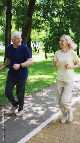 Senior couple jogging together on park path. Active mature man and woman running and smiling during outdoor workout on sunny summer day
