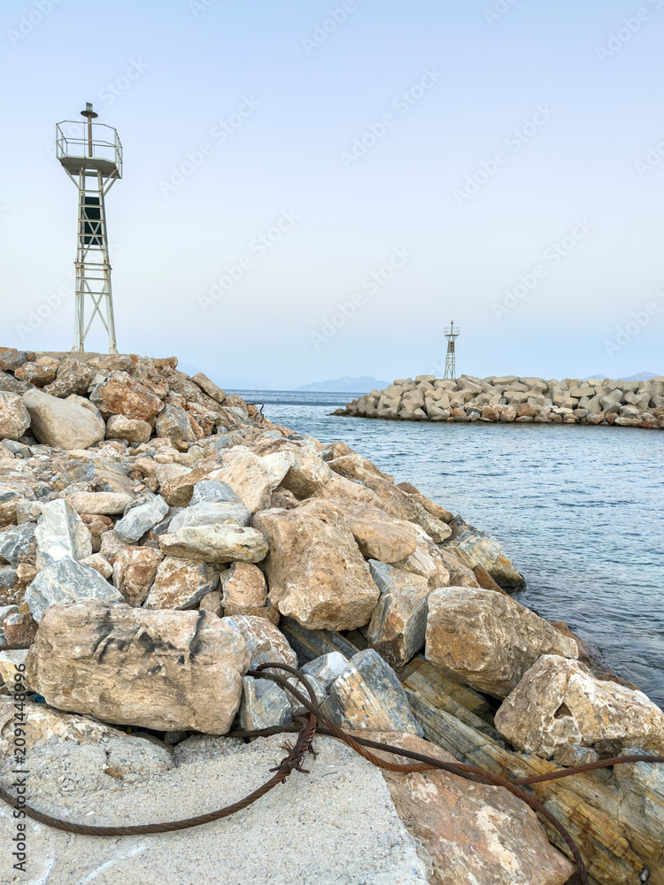 Fototapeta premium Lighthouses on rocky breakwaters at Agios Kirikos harbor, Ikaria island, Greece