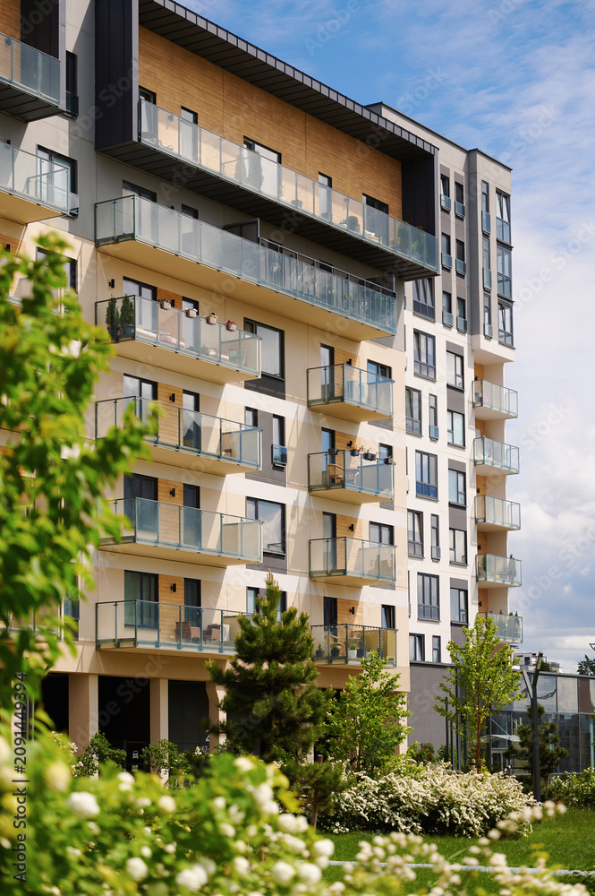 Fototapeta premium Modern apartment building with balconies and green surroundings on a sunny day.