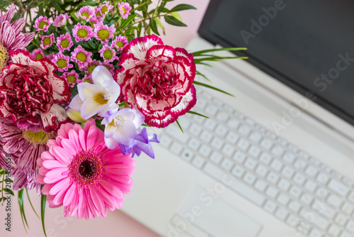 Bouquet of colorful flowers beside a laptop keyboard on a modern desk. Happy remote work combines productivity creativity and wellbeing in a home office.