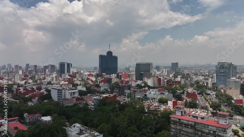 Aerial panoramic view of the Mexico City skyline looking south with modern skyscrapers, drone tracking sideways over the sprawling cityscape under a cloudy blue sky
