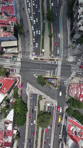 Vertical aerial top-down view of a busy urban intersection and underpass in Mexico City with the drone hovering over flowing traffic and tree-lined medians