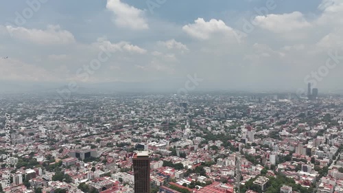High-altitude panoramic aerial view of the vast Mexico City skyline with the drone panning across the sprawling cityscape under a cloudy blue sky