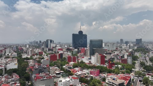 Aerial panoramic view of the Mexico City skyline looking south, drone rotating over sprawling urban buildings under a dramatic cloudy blue sky