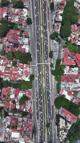 Vertical aerial top-down view of the Viaducto highway in Mexico City with heavy traffic flowing between dense residential neighborhoods and green trees