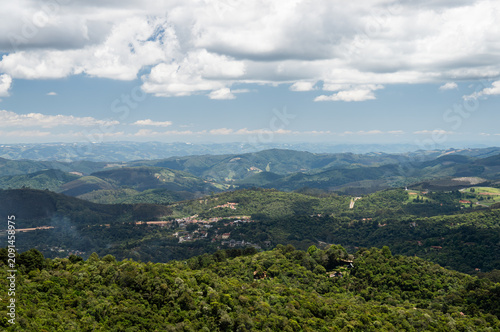 Panoramic view from Pedra Redonda rock summit with rolling green mountains of Serra da Maniqueira and dramatic cloudy blue sky above in Monte Verde, Camanducaia, Minas Gerais - Brazil