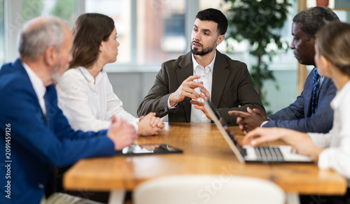Employees sit at a table in a modern office and discuss business development among themselves.