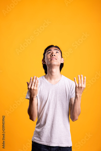 Bild auf Leinwand Hopeful Asian man looks upward with open hands raised in front of him, anticipating positive outcome and showing gentle pleading or wishing expression against isolated background