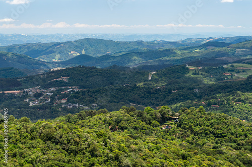 Panoramic mountain landscape with forest valleys and village under summer morning sunny blue sky and soft clouds scenery in Monte Verde, Camanducaia, Minas Gerais - Brazil