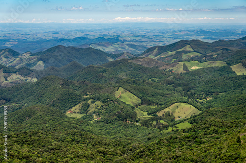 Rolling green hills and Atlantic Forest valleys seen from the summit of Pedra Redonda summit Monte Verde Highlands under summer morning sunny day. Monte verde, Camanducaia, Minas Gerais - Brazil.