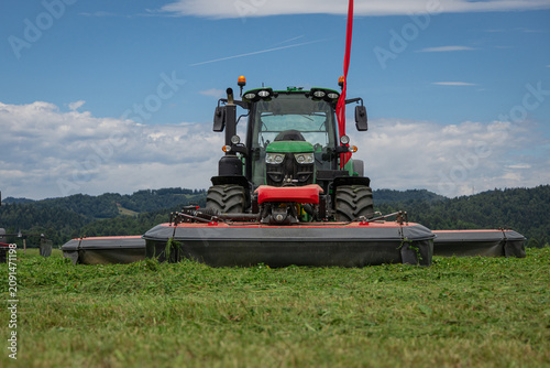 Tableau sur toile Front view of a modern tractor equipped with triple disc mowers harvesting fresh grass on a rural meadow