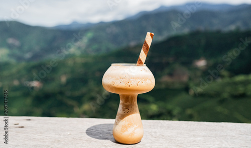 Foto Batido de café helado con espuma servido en copa de vidrio frente a paisaje de m