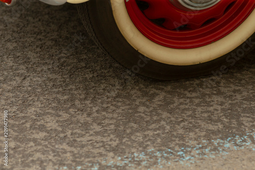 Obraz na plátně Low-angle view showing a vintage car wheel with a whitewall tire and glossy red steel rim resting on rough textured asphalt