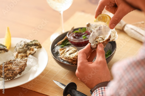 Foto Young man squeezing lemon on raw oyster at home, closeup