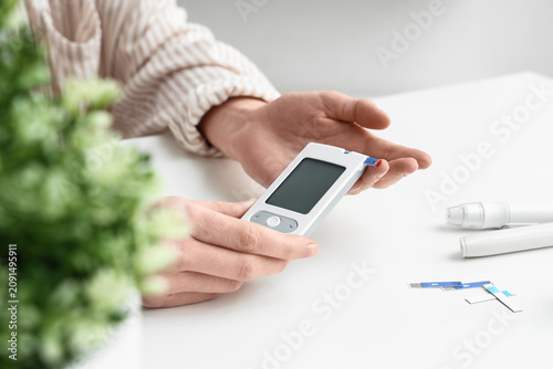 Photos Woman with digital glucometer at white table