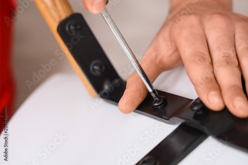 Fotografie Male carpenter tightening screw in chair with screwdriver, closeup