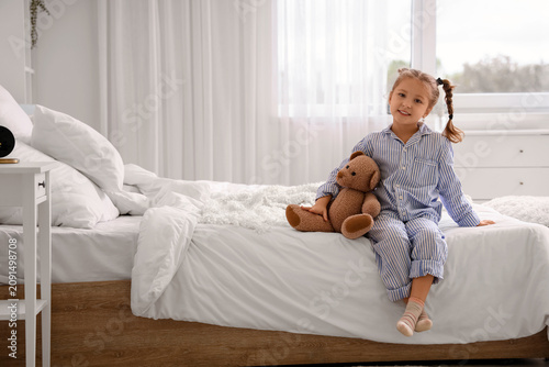 Cute little girl with toy bear in bedroom