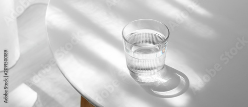 Valokuva Glass of water on a white table with natural light and shadow, Hydration and wel
