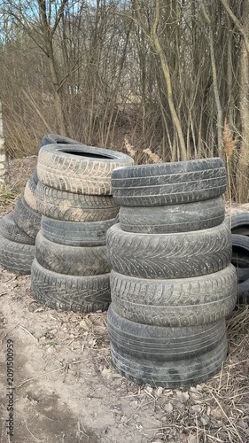 Stacked worn tires on gravel roadside. Birch trees background, columns of passenger car tires awaiting collection, weathered