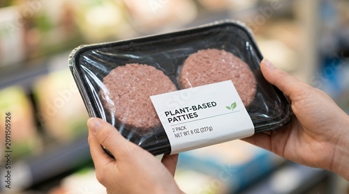 Hands holding a two pack of plant based burger patties in plastic packaging with a white label indicating nutritional information and a green leaf logo vegan vegetarian food