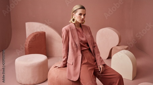 Stylish Woman in Pink Blazer and Pants Posing in Studio with Abstract Shapes