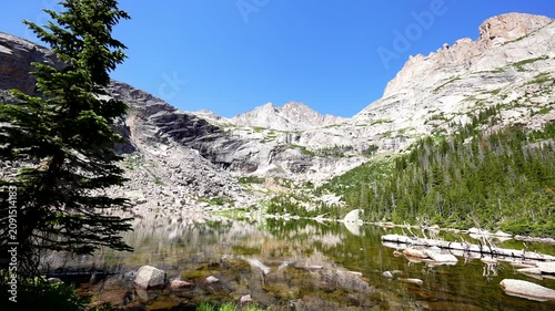 wide shot of beautiful rocky mountain lake in the RMNP colorado rockies Black Lake with reflection on clear glacial water and cloudless blue sky with audio
