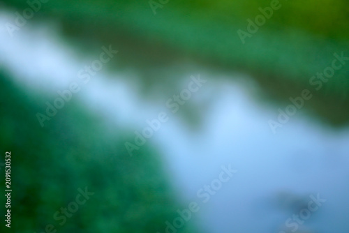 фотографія Abstract blurred nature background of a river stream and green vegetation, intentional out of focus bokeh backdrop of water flow on a sunny day with copy space
