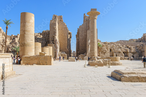 Tourists sightsee at the First Courtyard (or Forecourt) of the Karnak Temple Complex, located in Luxor, Egypt, with the Column of Taharqa and Colossal Statue of Ramesses II in view.