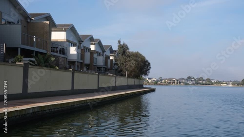 Modern waterfront townhouses line a boardwalk beside a calm suburban lake in Sanctuary Lakes, Point Cook, Melbourne Australia. Contemporary Australian waterside living.