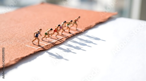 Miniature runners at starting line on textured track with long shadows business competition concept