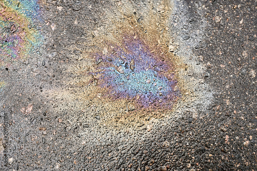 Oil Spill Creates Colorful Patterns on Pavement During a Sunny Day in a City Street.