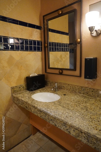 фотографія A public restroom or hotel bathroom vanity featuring a speckled granite countertop, an undermount white oval sink, and a chrome faucet