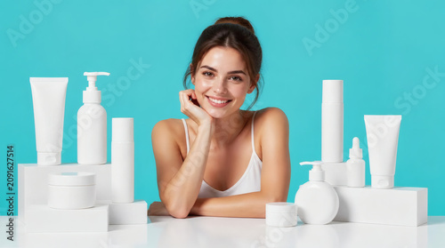 Young Woman Smiling with Skincare Products on Bright Blue Background