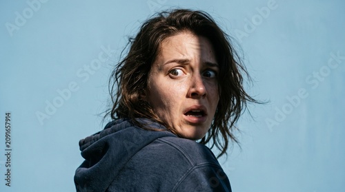 Woman with shocked expression looking over her shoulder against a blue background