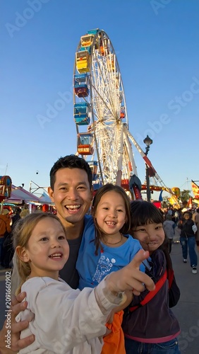 Man and Children Posing at an Amusement Park with a Ferris Wheel