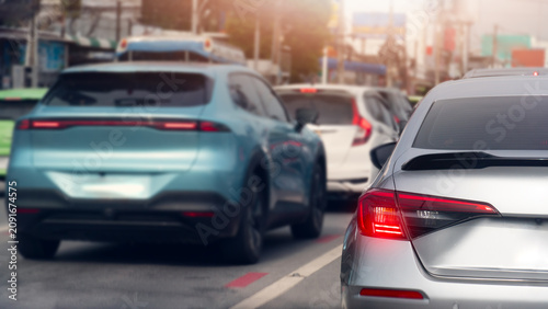 Low close up perspective of modern light blue and silver sedans bumper-to-bumper in an urban traffic jam. A bright lens flare illuminates the busy city street lane. Traiffic in Thailand at days time.