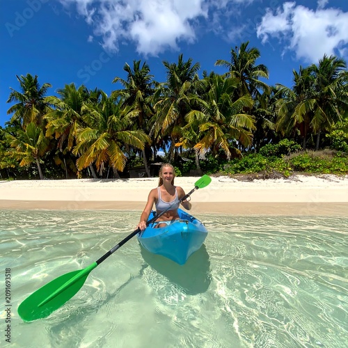 A Person Kayaking in Clear Water Near a Tropical Beach with Palm Trees
