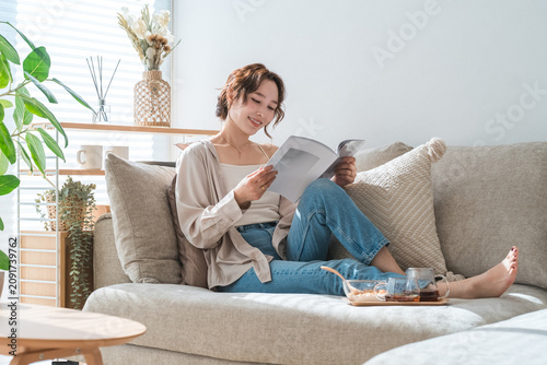 Foto A stylish Asian woman sitting on the living room sofa, reading a magazine during teatime