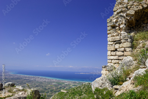 View from ancient ruins overlooking a coastal town and the sea under a clear blue sky.