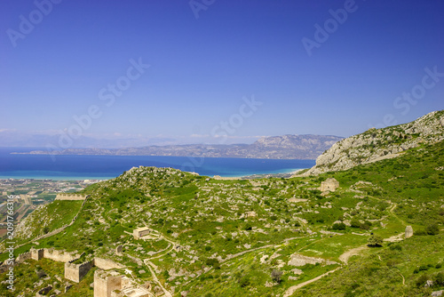 A panoramic view of the ancient ruins of Acrocorinth, Greece, overlooking the Gulf of Corinth on a clear day.
