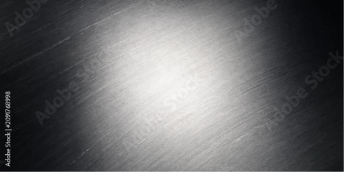 A close-up of a brushed metal surface with a bright spotlight in the center, creating a textured and industrial background.