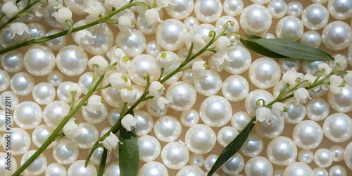 Flat lay of round white Akoya pearls mixed with lily of the valley sprigs densely filling frame soft natural light