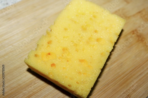 Foto Bright yellow cleaning sponge with porous texture placed on a natural wooden cut